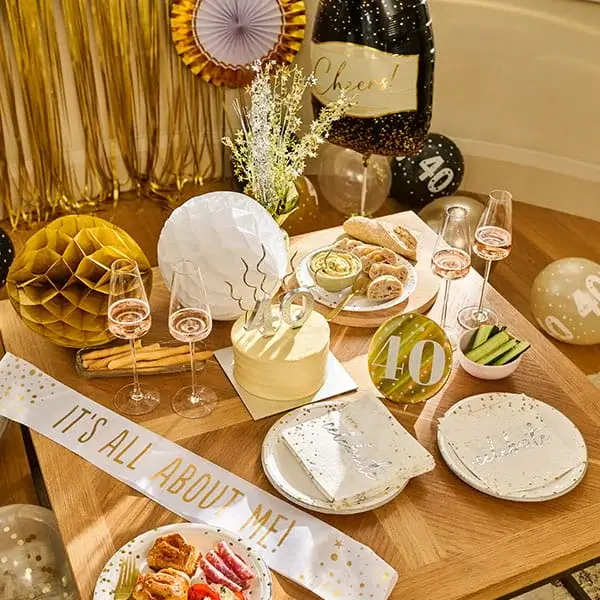 40th birthday celebration table with a cake, champagne glasses, gold decorations, balloons, snacks, and black-and-gold party décor.